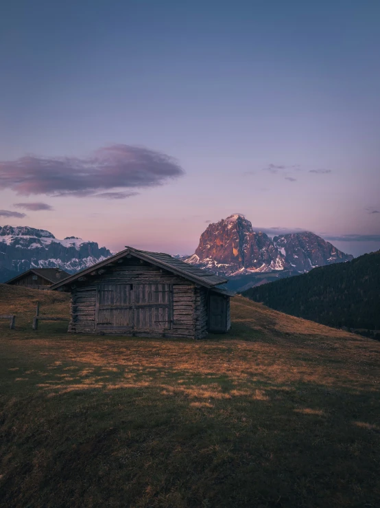 a wooden house in a grassy field near mountains