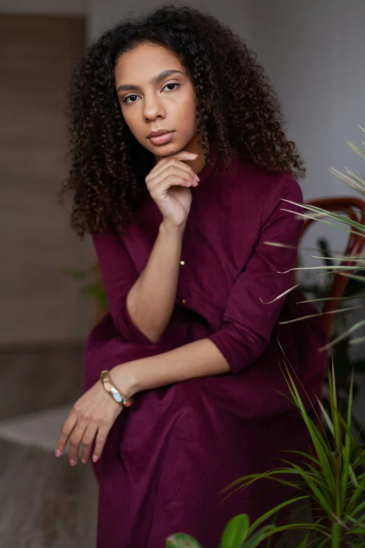 a young woman sits with her hands on her chin, looking directly at the camera