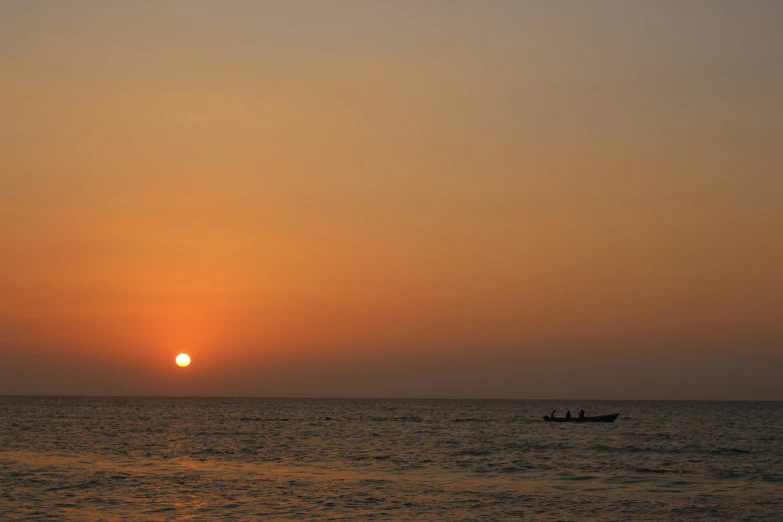 the sunset on the ocean with two small boats in the water