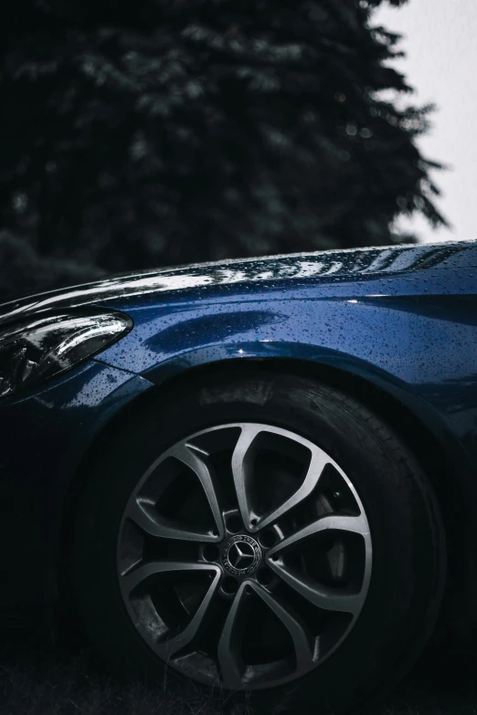 blue sport car parked in front of a tree with the hood up and snow falling on it