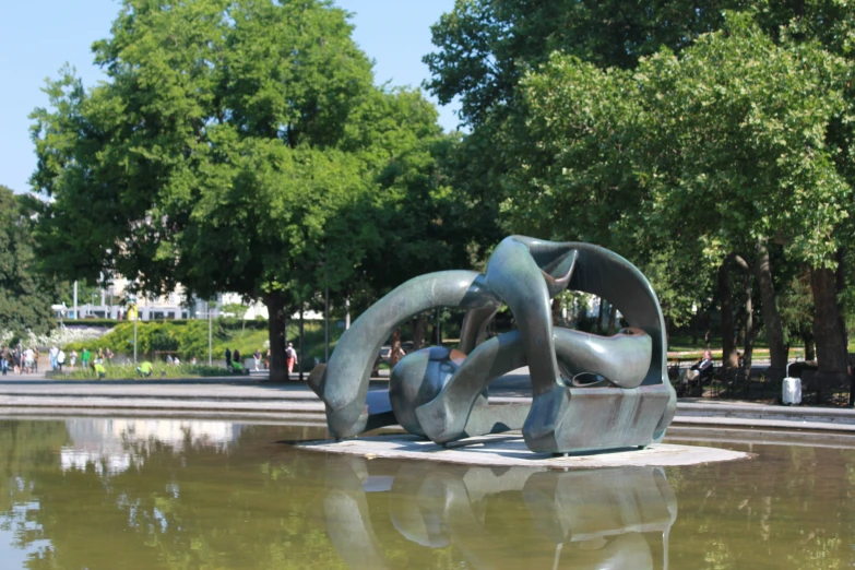 a metal sculpture near the water with trees behind it