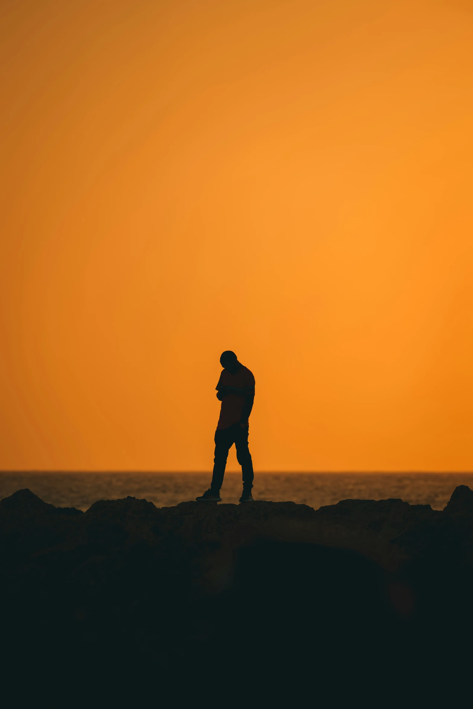 man standing on top of rocks watching the sun go down