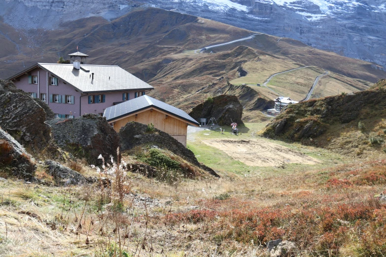 a pink house on a mountain with some snow capped mountains in the background