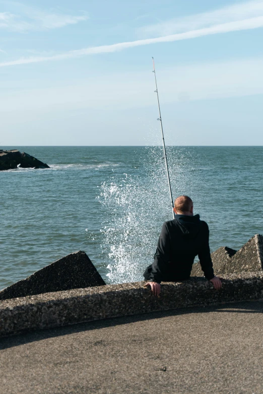 a man sits on a wall next to a fishing pole