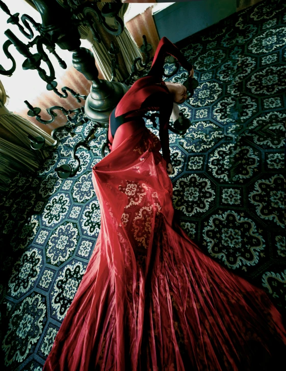 a woman in an elegant red dress stands by a chandelier