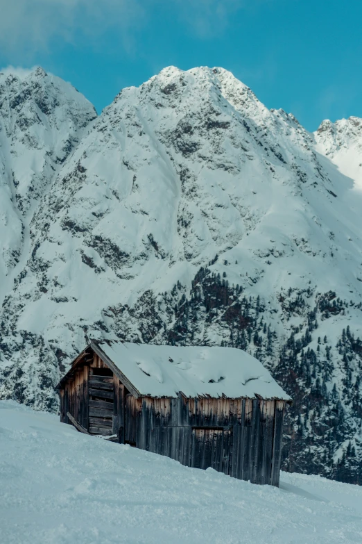 a cabin sits on a snowy hillside in front of some mountains