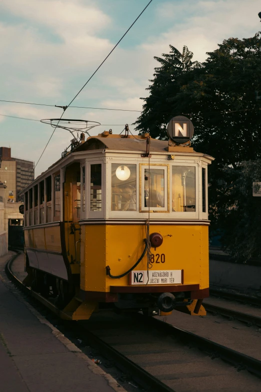 a yellow trolley train traveling down tracks past trees