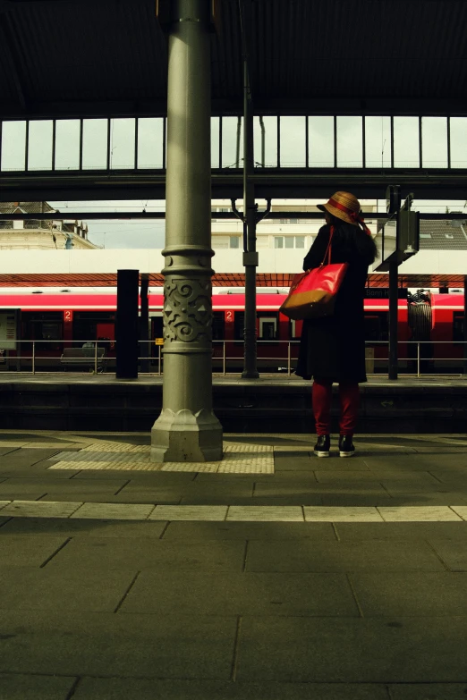 a woman holding a bag on the platform as a train goes by