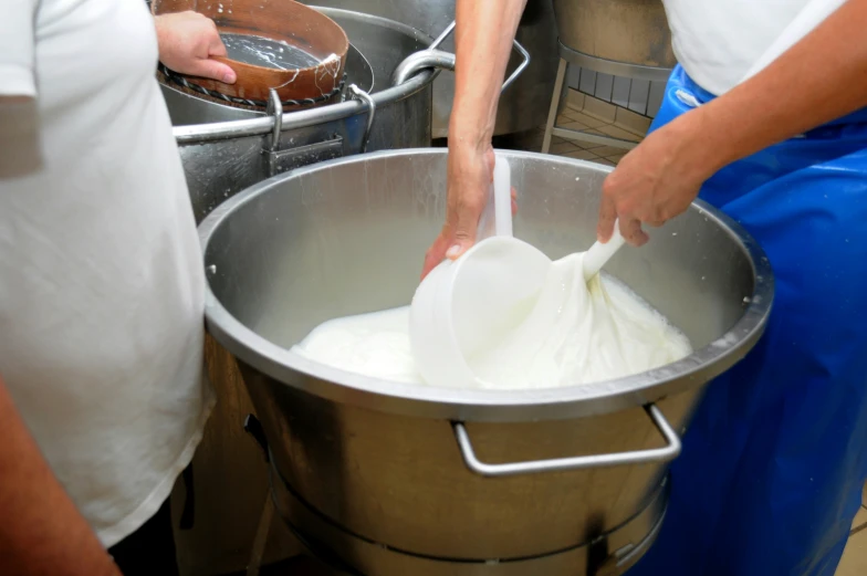 two people pouring milk into a large metal bowl