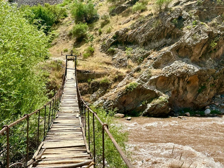 a wooden bridge spanning across a river with mountains in the background