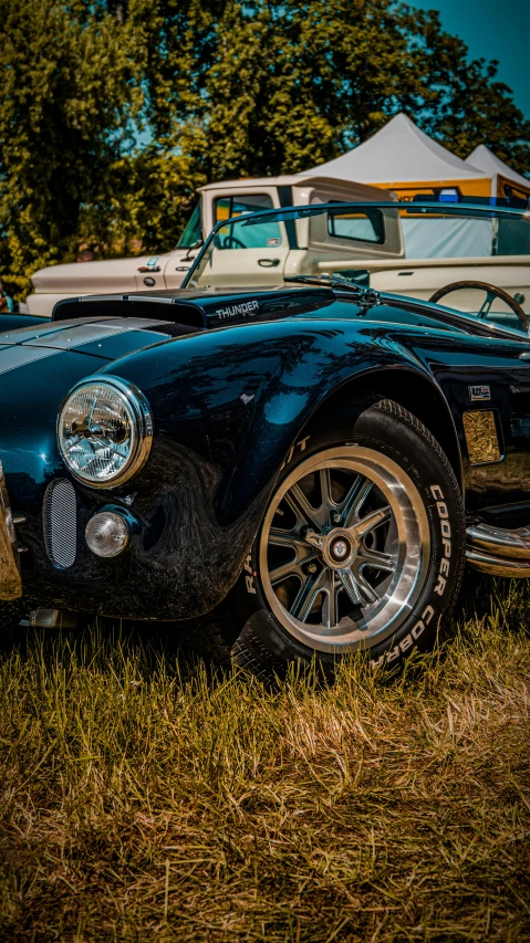 a vintage car sitting in the grass next to a tent