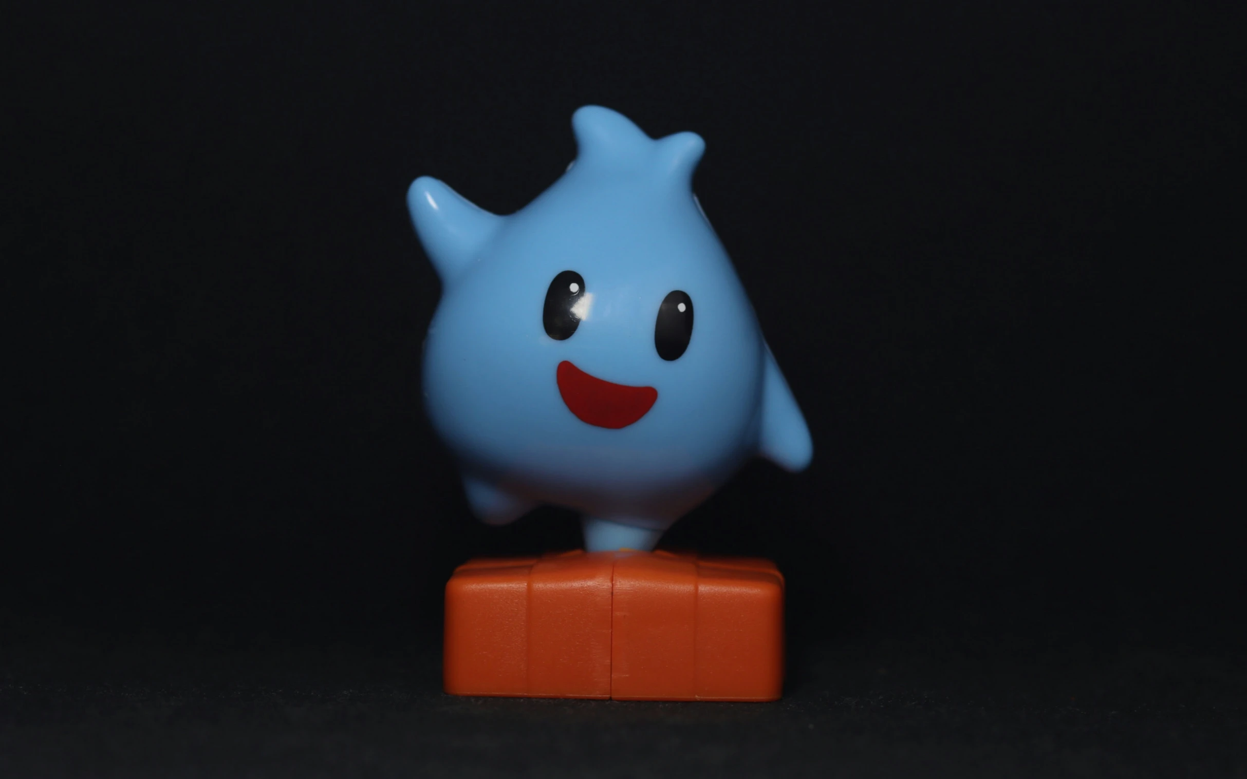 a blue plastic character with eyes and tongue protruding out from the corner