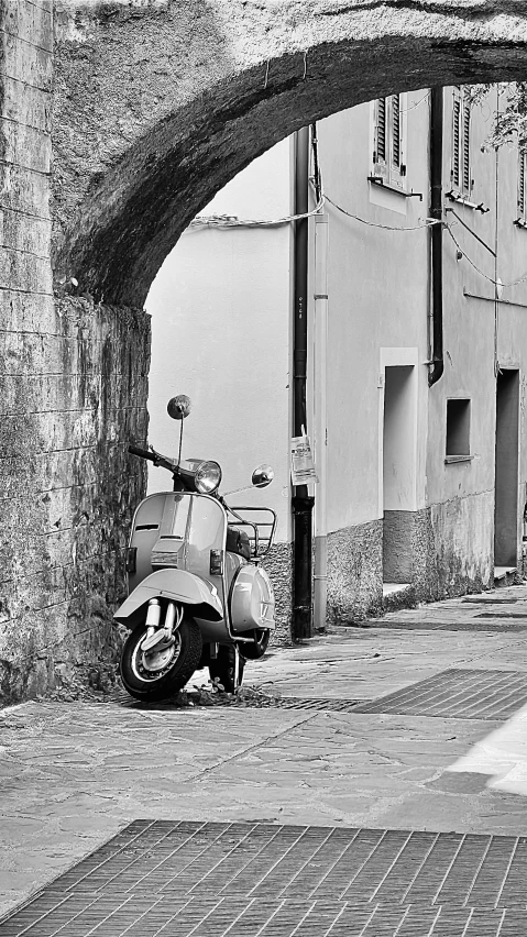 an empty street with a scooter parked by an archway