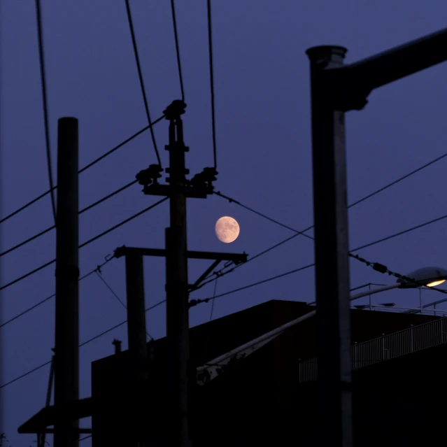 the moon is visible over some power lines