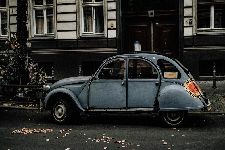 an old blue car is parked in front of a large building