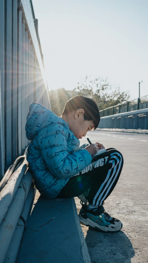 a young man is sitting by the side of a wall and writing