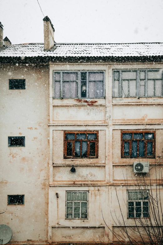 this is an old building with windows and a roof with snow falling on the ground