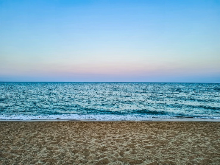 the sun is setting on a beach with the water lapping on