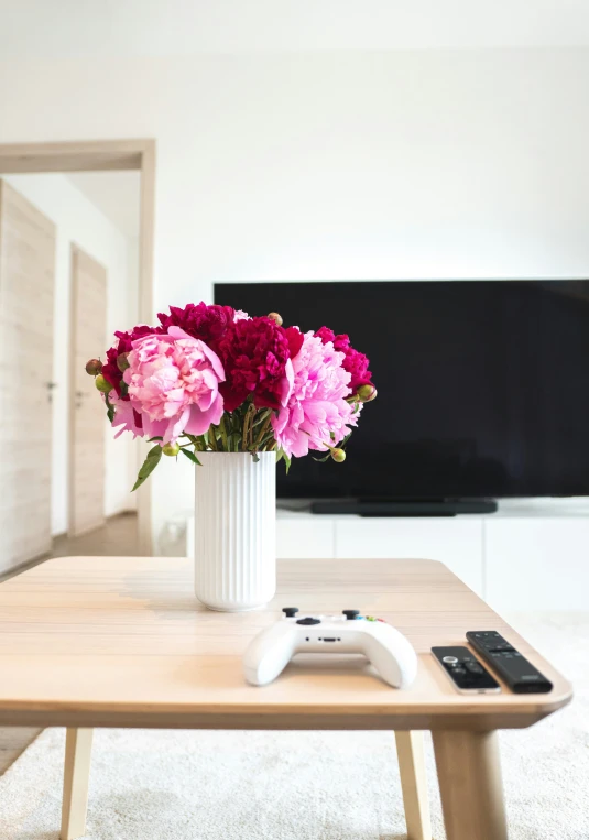 a white vase with flowers and remote controls sits on a table