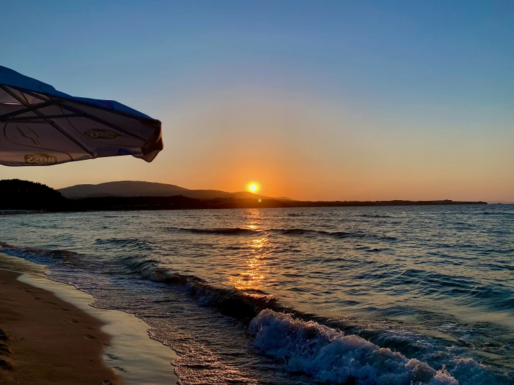 there is an umbrella that is on the beach at sunset