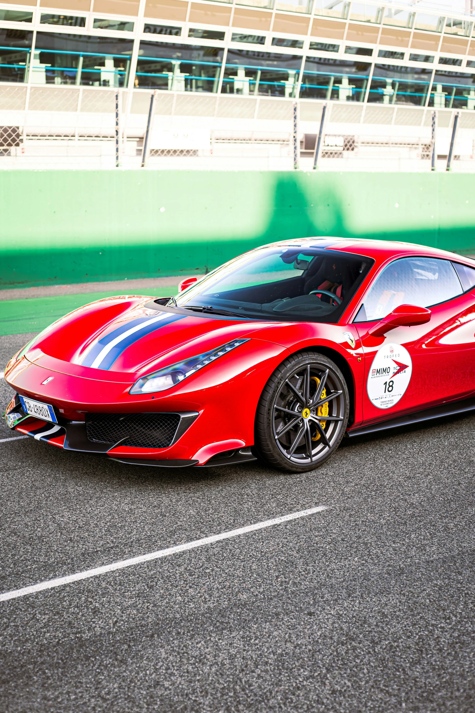 a red ferrari on a track with grass and building in the background