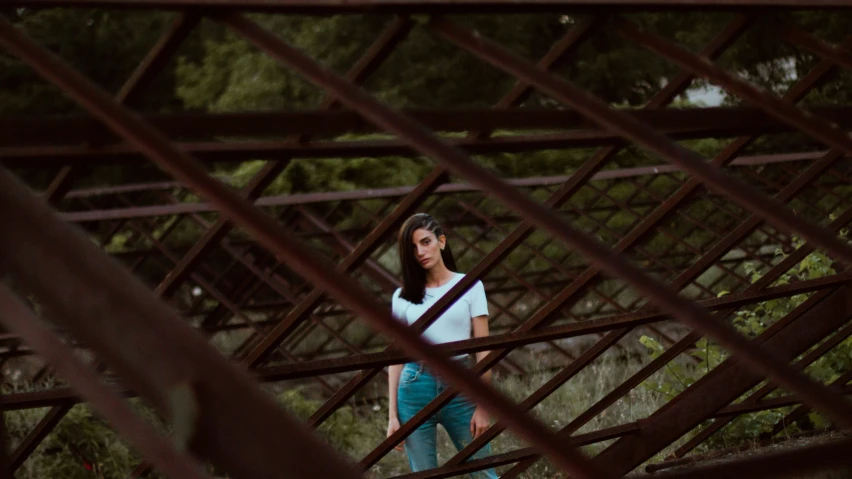 a girl standing outside looking through an old rusty cage