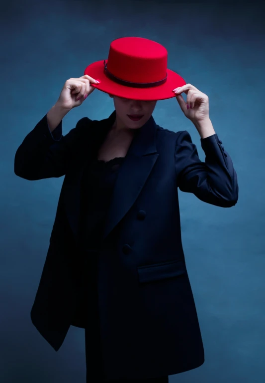 a woman in a black suit and red hat poses with her hands on her head