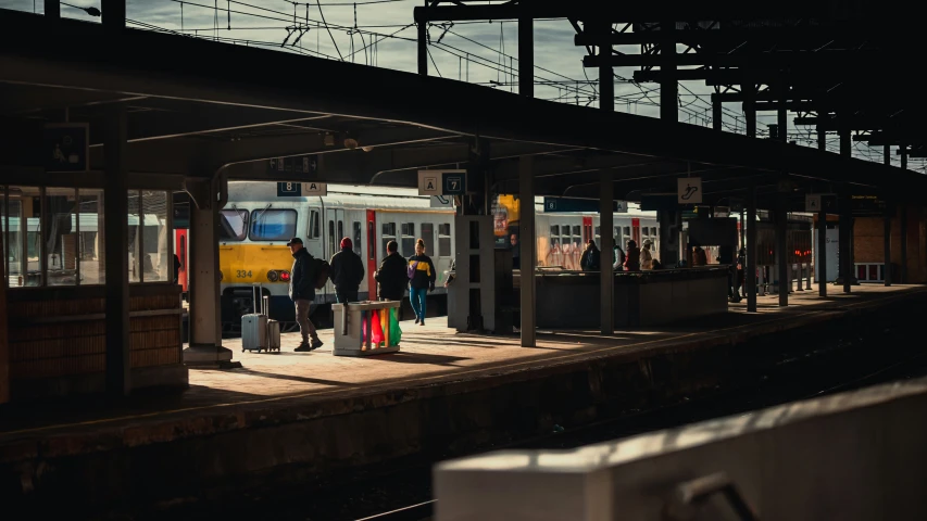 people at a train station standing near a yellow and white passenger train