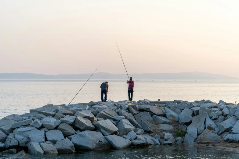 two people fishing off of a large rock jetty