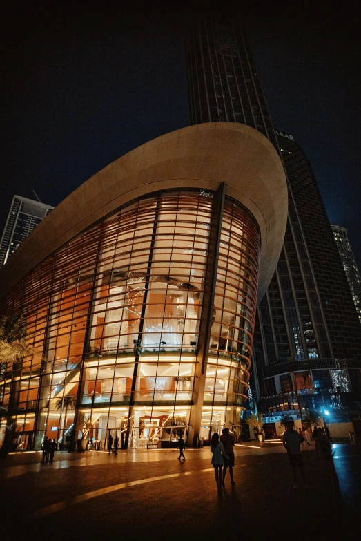 a building lit up at night with people walking around it