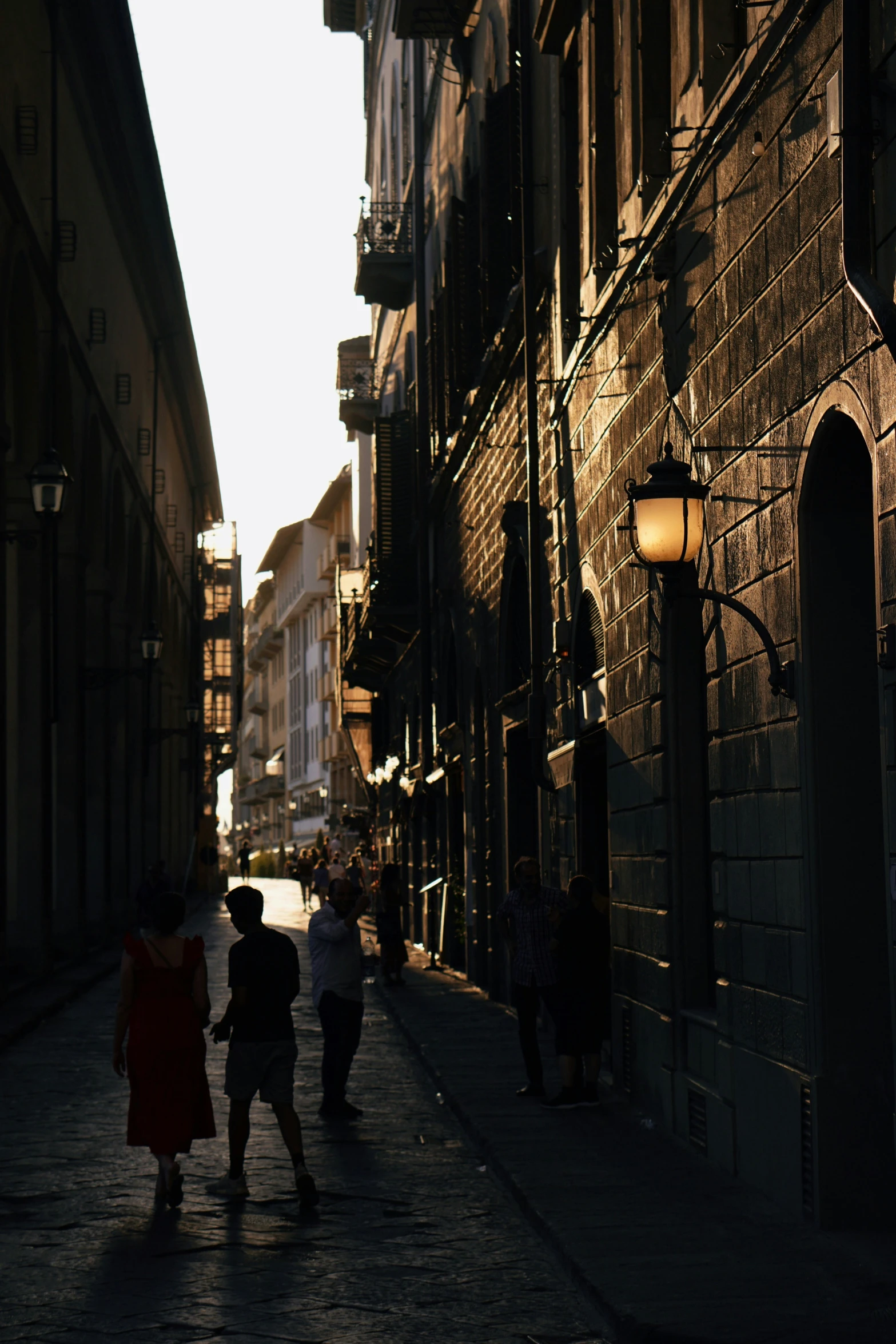 people walking down a narrow street next to a street light