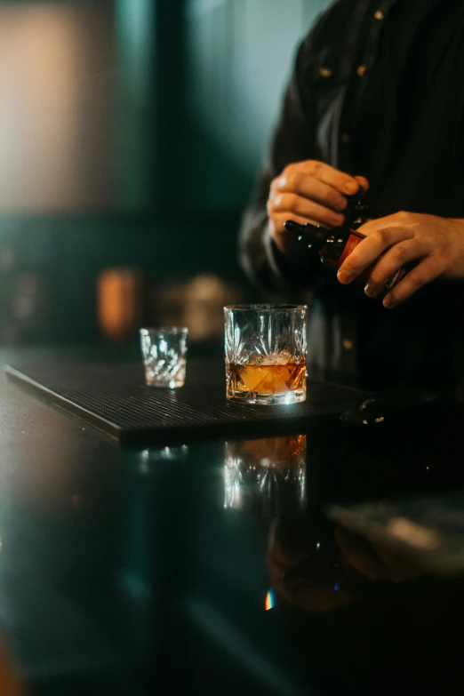 someone pouring whisky into a glass sitting on a bar