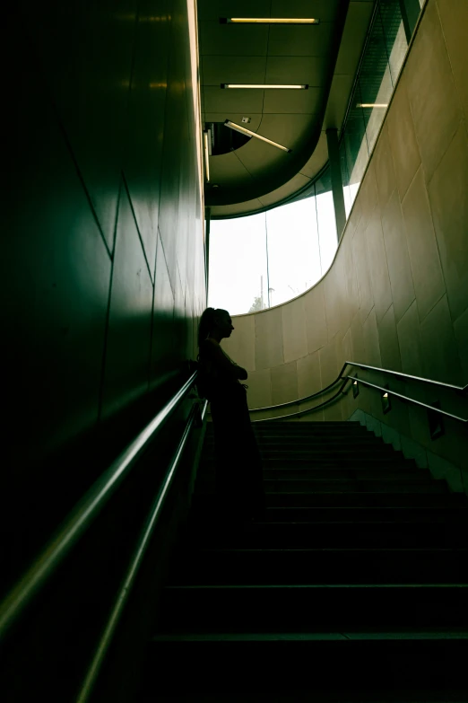 person standing in tunnel looking down staircase at light
