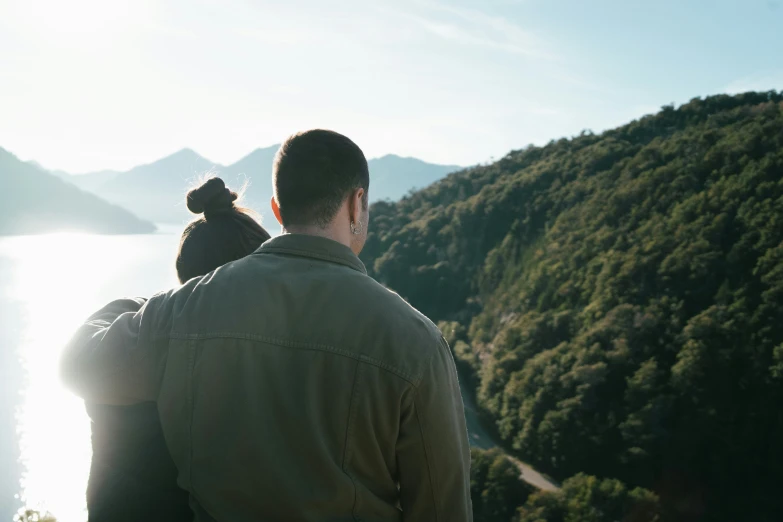 a man holds his little child and looks over a lake