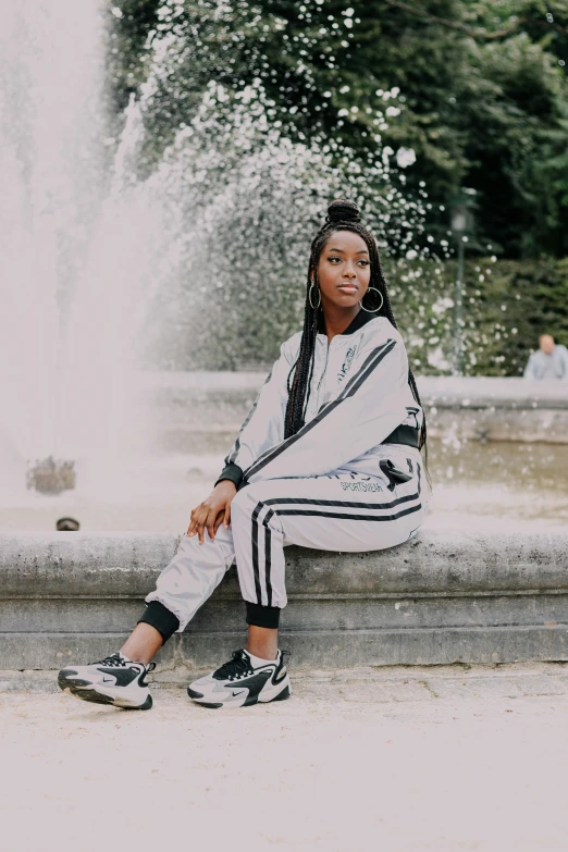 black woman sitting against a fountain wearing adidas and a hoodie