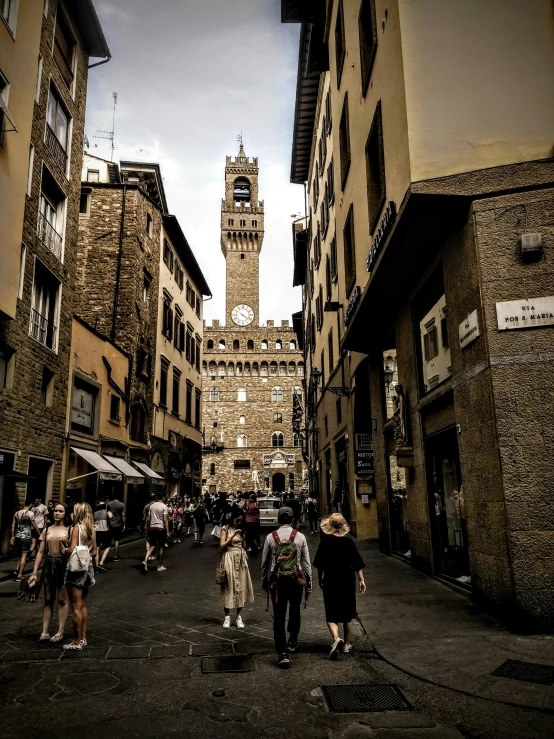 a street in a historic italian village with people on the sidewalks and a clock tower