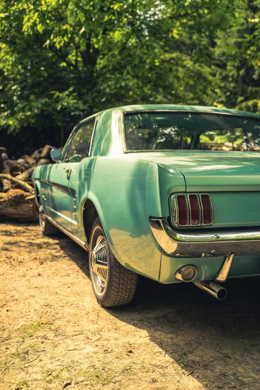 a blue mustang sits parked in the sand in front of some trees