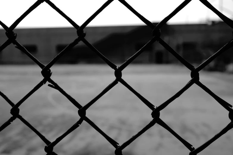 black and white pograph of an empty building through a chain link fence