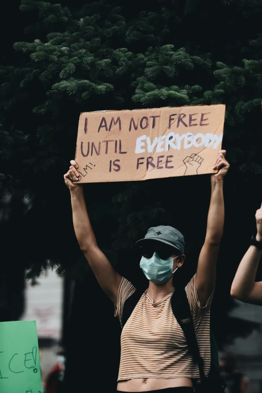 a woman with a face mask holding a sign that says i am not free until everybody is free