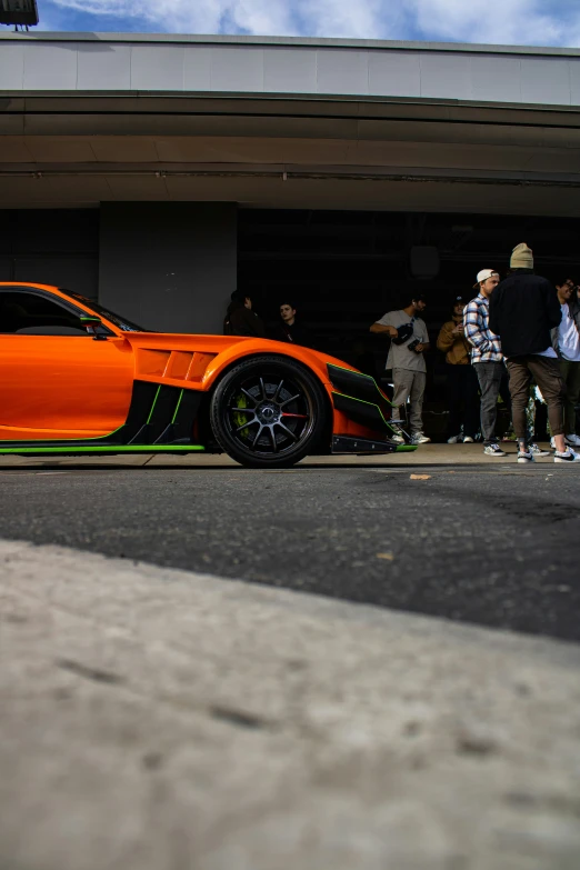 the sporty orange sports car sits parked next to its owner