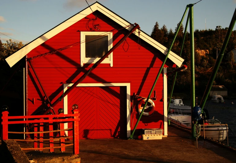 the boat is docked to the red shed by the water