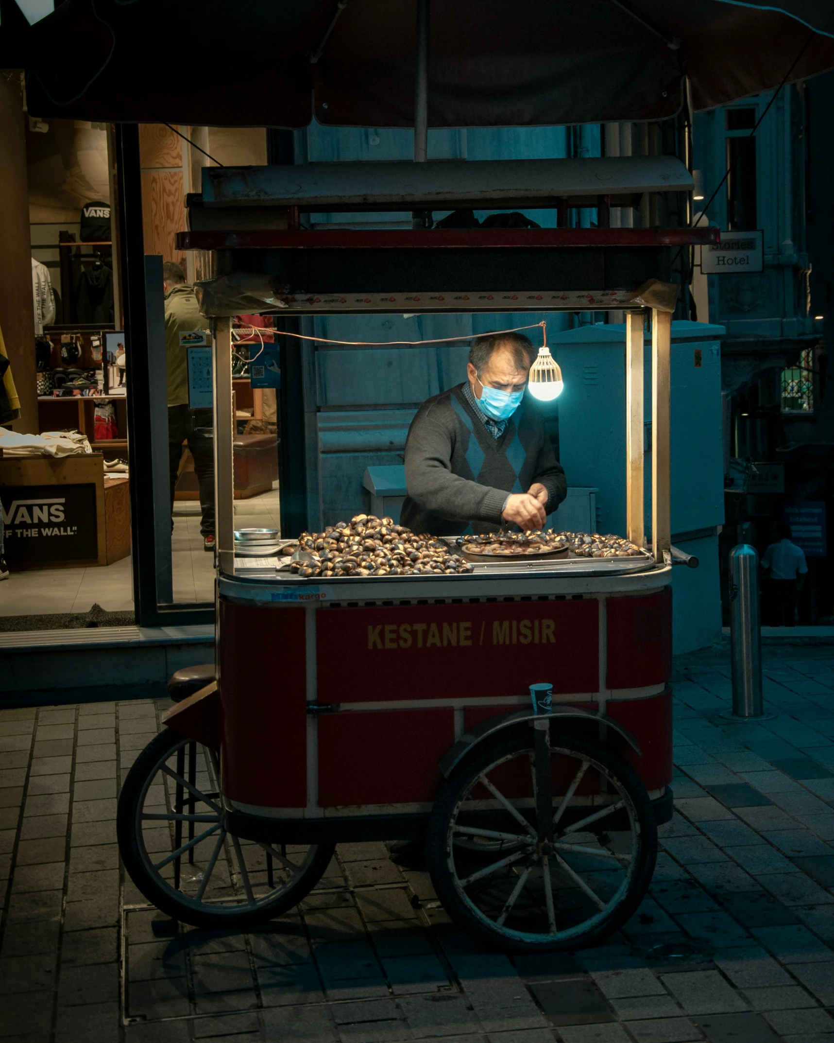 a man wearing a mask is behind a street food stand