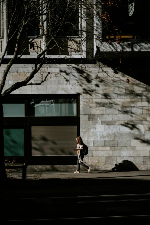 a young woman walking by a tall wall on a street