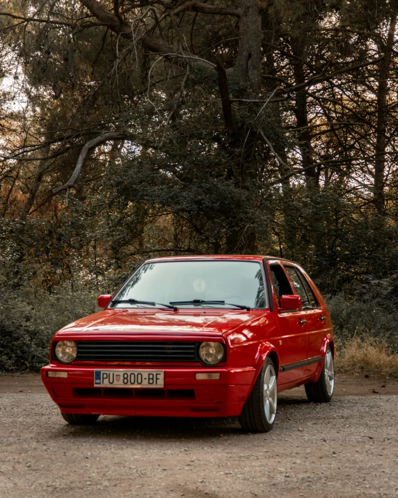 an orange car parked on the side of a dirt road near trees