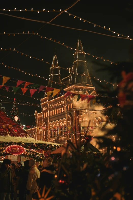 people walking around at an outdoor market decorated with lights