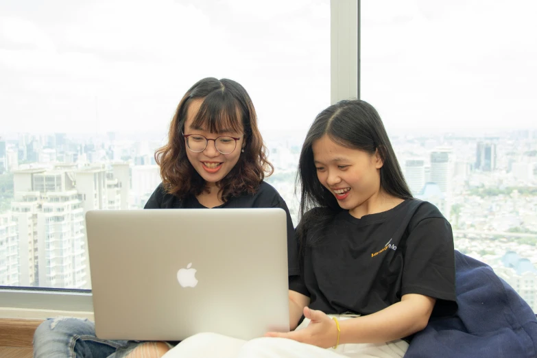 the woman and girl are sitting by the window using their laptops