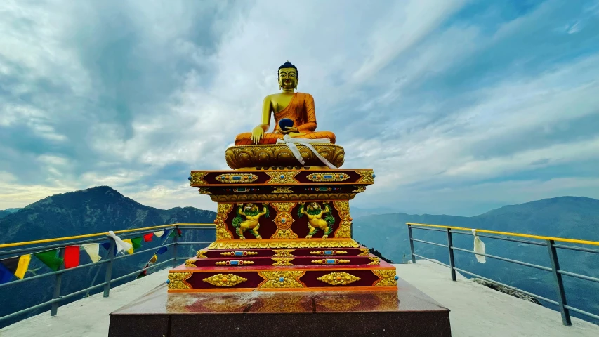 a statue on a ledge with mountains in the background