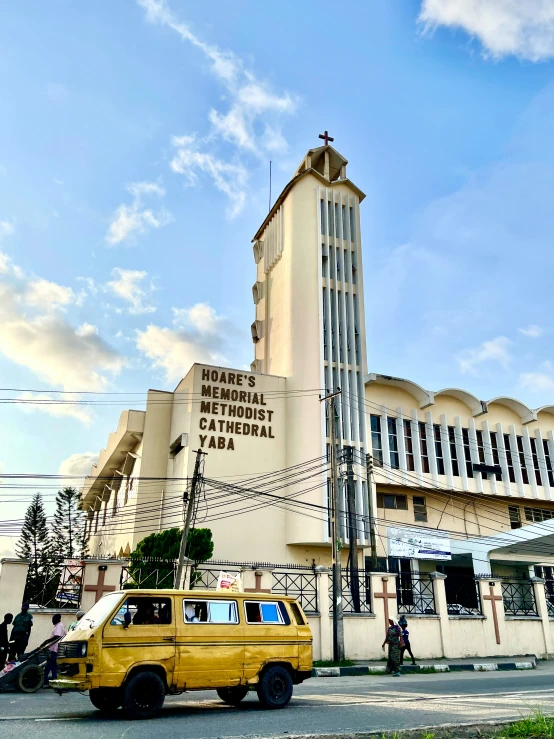 a yellow taxi driving past a building with a tall tower