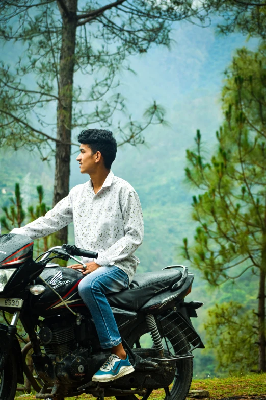 a person sitting on a parked motorcycle with a wooded area in the background