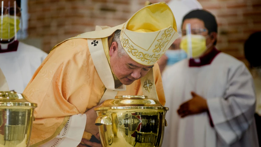 priest in orange outfit and white hat placing a golden vase on it